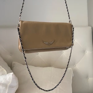 Zadig väska  - Intressekoll! En superfin väska från Zadig Voltaire i en beige/rosa färg. Kommer inte till användning längre. Den är använd sparsamt, men baksidan är lite sliten som man kan se på en av bilderna. 