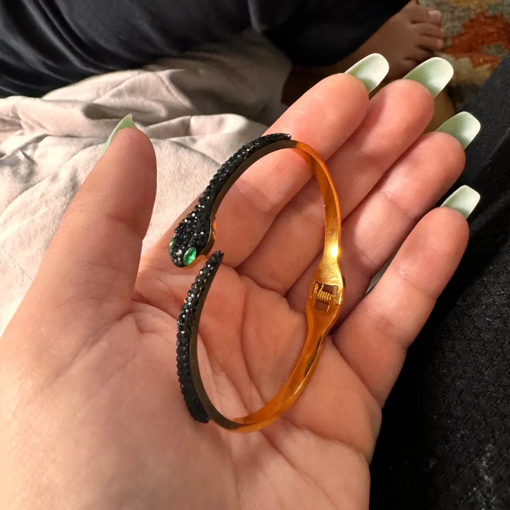 Säljer ett helt nytt coolt armband i form av en orm. Armbandet är i guld med svarta detaljer och har gröna ögon som verkligen poppar! Perfekt för att ge din outfit en edgy touch. Passar både till vardags och fest.. Accessoarer.