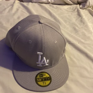 Grå New Era 59FIFTY keps - Säljer en grå New Era 59FIFTY keps med LA-logga i vitt framtill. Kepsen är i mycket bra skick och har en klassisk passform. Perfekt för både vardag och sportiga tillfällen. Har ej använt den för det är för stor.