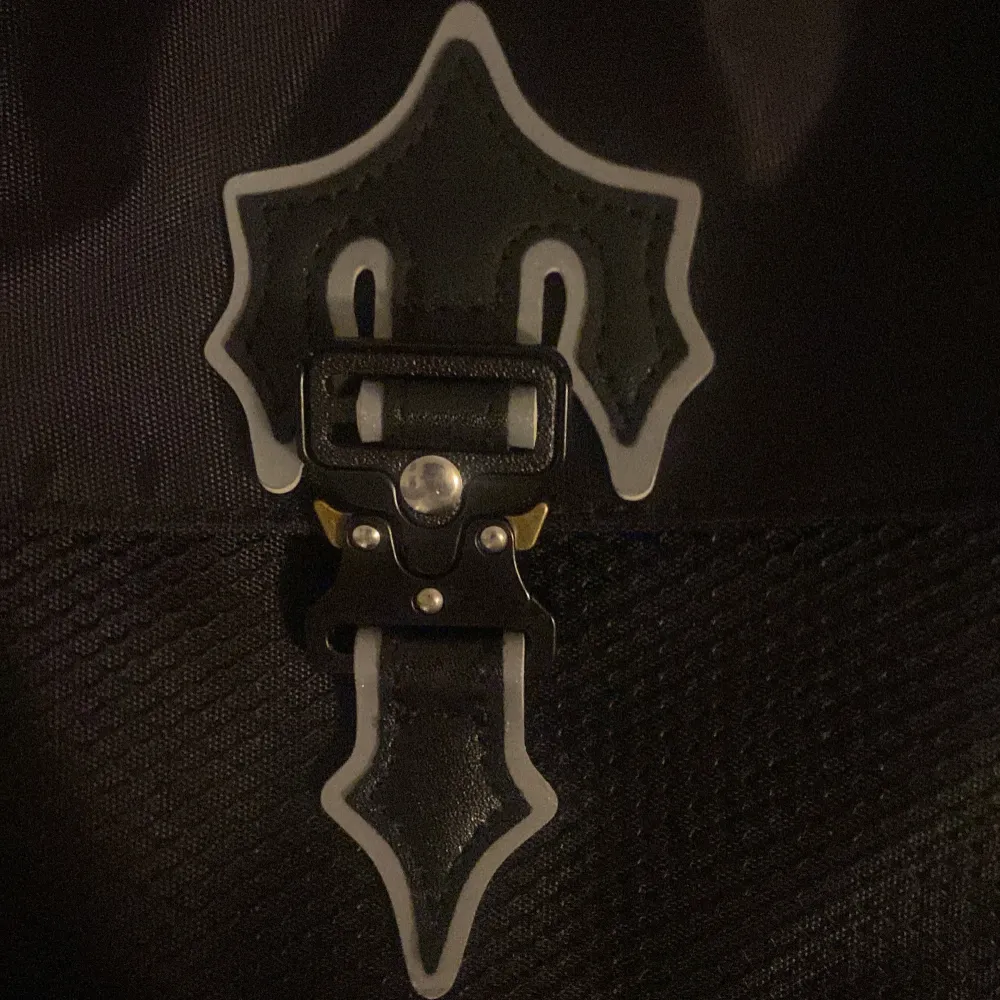 Snygg svart axelväska från Trapstar med en cool spänndetalj på framsidan. Väskan är perfekt för vardagsbruk och har en justerbar axelrem. Den är gjord i ett slitstarkt material och har en unik design som verkligen sticker ut. Perfekt för att ge din outfit en edgy touch!. Laukut & Käsilaukut.