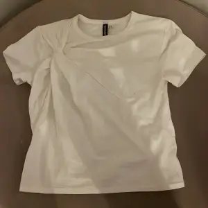 Säljer en stilren vit t-shirt från H&M i storlek XS. Den har en unik draperad detalj på framsidan som ger en snygg twist till en klassisk look. Perfekt för både vardag och fest! 💫