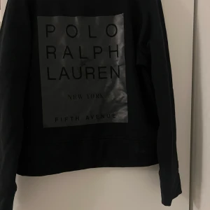 Svart tröja från Polo Ralph Lauren - Säljer en snygg svart tröja från Polo Ralph Lauren med ett stort tryck på framsidan. Perfekt för en stilren look, oavsett om du ska ut på stan eller bara chilla hemma. Tröjan är i bra skick och passar perfekt till jeans eller chinos. Skicka ett meddelande vid intresse!