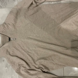 Beige half zip - Säljer en stilren beige tröja med dragkedja framtill. Perfekt för både vardag och lite finare tillfällen. Tröjan har långa ärmar och är i ett mjukt material som känns skönt mot huden. Passar bra till höst och vår.