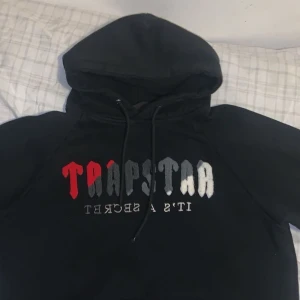 Svart hoodie från Trapstar - Säljer en svart hoodie från Trapstar i storlek M hade passat Sockså . Den har en cool textdesign i rött, grått och vitt på framsidan. Perfekt för höst och vinter med sin mysiga känsla och långa ärmar. Passar både till vardags och chillkvällar.