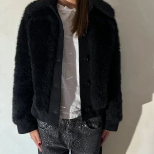 Svart pälsjacka - Säljer en supermjuk och fluffig svart pälsjacka med knappar framtill. Perfekt för att hålla sig varm och stilren under kyliga dagar. Jackan har en klassisk krage och långa ärmar, vilket gör den idealisk för både höst och vinter. Passar perfekt till både vardag och fest!