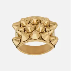 Cool och edgy guldfärgad ring med nitar i ett geometriskt mönster. Perfekt för att ge din outfit en tuff touch. Ringen är i mycket bra skick inga repor 