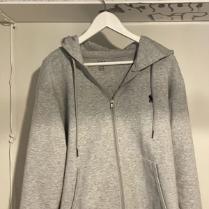 Grå hoodie från Ralph Lauren - Säljer en snygg och bekväm grå hoodie från Ralph Lauren. Den har en dragkedja framtill och en klassisk broderad logga på bröstet. Mycket bra skick. Perfekt för en avslappnad stil och passar till alla årstider. 🐎