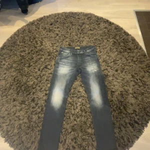 Grå jeans från Jack & Jones - Säljer ett par grå jeans från Jack & Jones i bra skick. De har en snygg slitning på framsidan och en klassisk femficksdesign. Perfekta för en casual look!