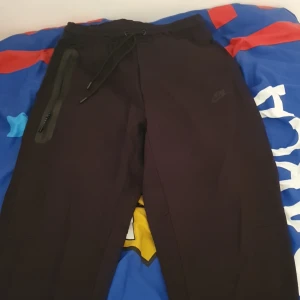 Helt ny oanvänd svart nike tech byxor - Säljer ett par svarta mjukisbyxor från Nike i storlek M. Byxorna har en dragkedja på sidan och snörning i midjan för bästa passform. Perfekta för en avslappnad stil eller träning. De är i mycket bra skick och redo för nya äventyr! Passar både M och l!