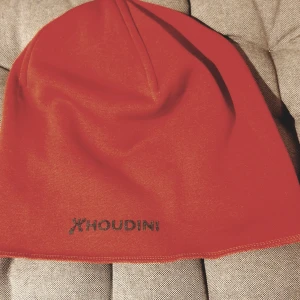 Mössa från Houdini - Säljer en snygg röd mössa från Houdini i fleece. Perfekt för kalla dagar med sin mjuka och varma känsla. Den har en enkel design med Houdini-loggan broderad framtill. Passar både till vardags och utomhusaktiviteter. 🧢