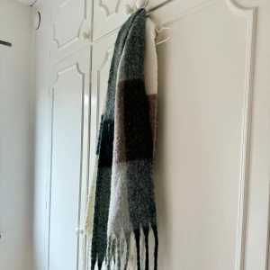 Mjuk flerfärgad halsduk - Säljer en supermjuk och mysig halsduk i flera färger som grönt och beige. Perfekt för kalla dagar med sitt fluffiga material och stilrena rutmönster. Den har fransar i ändarna som ger en extra touch. Passar perfekt för höst och vinter!
