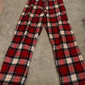 Röda rutiga byxor - Säljer ett par mysiga röda rutiga byxor i storlek 146/152. Perfekta för en avslappnad dag hemma eller som pyjamasbyxor. De har en klassisk rutig design i rött, vitt och svart. Superbekväma och stiliga!