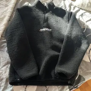 Mysig svart fleece tröja från Jack and Jones, perfekt för kyliga dagar. Den har en halv dragkedja framtill och en hög krage för extra värme. Tröjan är i mycket bra skick och passar perfekt för både vardag och utomhusaktiviteter. Ett måste för höst- och vintergarderoben!