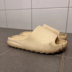Beiga tofflor strl 40 - Säljer ett par bekväma beige sandaler i syntetmaterial. Perfekta för sommaren med en enkel och stilren design. De har en öppen tå och en tjock sula som ger bra stöd. Använda men i ganska bra skick.