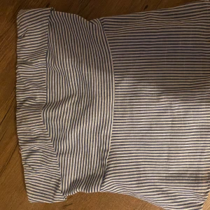 Randig topp - Säljer en superfin randig topp i blått och vitt. Toooen har en dragkedja baktill och en bred linning som ger en snygg passform. . Den är i bra skick och redo för nya äventyr!