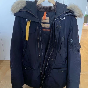 Blå vinterjacka från Parajumpers - Säljer en blå  Parajumpers vinterjacka i medium. Den har en snygg pälsfodrad huva och flera praktiska fickor. Jackan är i mycket bra skick och perfekt för kalla vinterdagar. Den har både dragkedja och knappar för extra skydd mot kylan. Pris kan diskuteras vid snabb affär! Herr model 