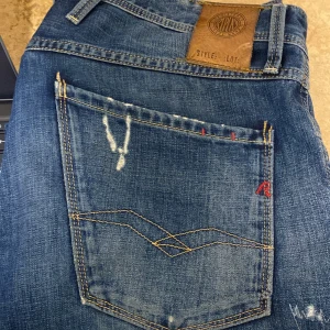 Replay - Säljer ett par snygga blå jeans från Replay med slitna detaljer och en cool vintage-look. De har en klassisk femficksdesign och är perfekta för en avslappnad stil. Passar både till vardags och fest! Skriv om ni har några funderingar!!!