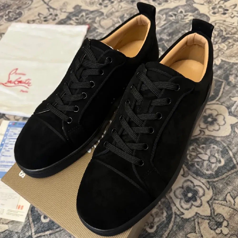 Säljer ett par snygga svarta sneakers i mocka från Christian Louboutin. De har den ikoniska röda sulan och svart snörning. Perfekta för både vardag och fest! Skorna är i nytt skick och kommer med originalförpackning.. Skor.