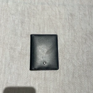 Svart plånbok från Montblanc - Säljer en elegant svart plånbok från Montblanc i skinn. Den har en stilren design med Montblanc-loggan på framsidan. Perfekt för att hålla dina kort och kontanter organiserade. Passar både till vardags och fest!