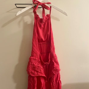 Rosa sommarklänning med volanger - Säljer en superfin rosa klänning perfekt för sommaren! Den har volanger och en härlig, luftig passform. Klänningen är ärmlös och har en knytning vid nacken. Perfekt för en dag på stranden eller en somrig fest! 🌞