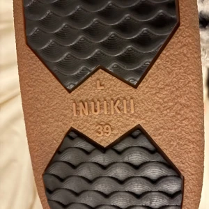 Beige Inuikii boots med paljetter - Säljer ett par snygga bruna Inuikii boots i storlek 39, men är som ett par 38:or. De har en mysig pälsfodring och är dekorerade med glittriga paljetter. Perfekta för vintern med sin varma och bekväma design. Snörning framtill för en bra passform. 