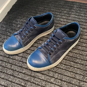 Blå sneakers från Lanvin - Snygga blå sneakers från Lanvin med snörning och en stilren design. Skorna har en vit sula och är tillverkade i mocka, vilket ger en lyxig känsla. Perfekta för en casual look. Storlek UK 6 vilket motsvarar storlek 40 (skulle däremot säga att de är lite stora i storleken). Priset går att diskutera! Skick: 7/10. Box och dustbag medföljer! Hör av er vid minsta lilla funderingar! 