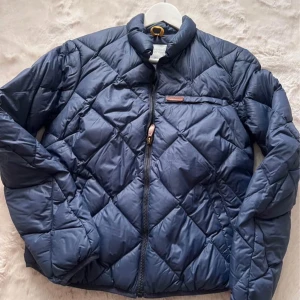 Blå quiltad jacka fr Peak Performance  - Snygg blå quiltad jacka med dragkedja och en liten bröstficka. Perfekt för kyligare dagar i vår och höst men även sommardagar, med sin vadderade design. Jackan har en stilren look och är lätt att matcha med olika outfits. Den är av en kortare modell Storlek Medium 