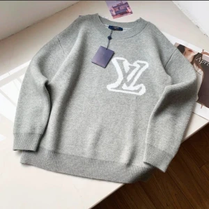 Grå tröja med logotyp - Snygg grå tröja med en stor vit logotyp på framsidan. Tröjan har långa ärmar och ribbade muddar vid ärmslut och nederkant. Perfekt för en stilren och avslappnad look.