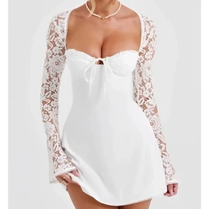 Studentklänning  - Elegant vit klänning med långa spetsärmar och snörning i ryggen. Den har en kort längd och en söt knytning framtill. Perfekt till studneten! 