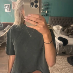 Grå/svart croppad t-shirt - Säljer en grå croppad t-shirt med korta ärmar. Perfekt för en avslappnad stil. Passar bra till jeans eller shorts.