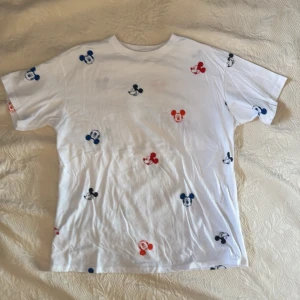 Vit t-shirt med färgglada tryck - Säljer en vit t-shirt med färgglada tryck i blått, rött och svart. T-shirten har korta ärmar och ett lekfullt mönster med små tryck över hela plagget. Perfekt för en avslappnad stil!