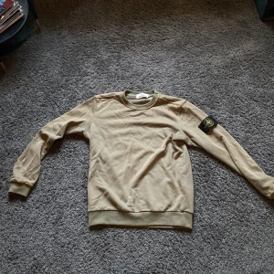 Olivgrön sweatshirt från Stone Island - Säljer en stilren grön sweatshirt från Stone Island med deras ikoniska märke på ärmen. Tröjan har rund hals och långa ärmar, perfekt för en avslappnad look. Passar bra till både jeans och chinos. OBS vet ej om äktenhet då tröjan var en present