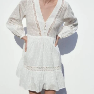 Vit klänning Zara med spetsdetaljer - Charmig vit klänning med v-ringning och spetsdetaljer. Klänningen har långa ärmar och knappar framtill. Perfekt för sommaren eller studenten❤️(OBS! knapparna på ärmarna är tyvärr borta, se bild 2)