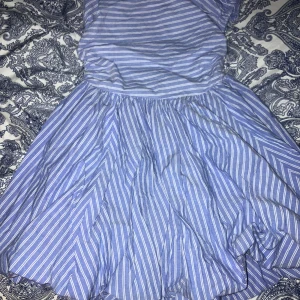Blå- och vitrandig klänning från Star - Charmig blå- och vitrandig klänning från Star med en luftig kjol och ärmlös design. Perfekt för varma dagar med sin lätta och bekväma passform. Klänningen har en elastisk överdel för extra komfort.