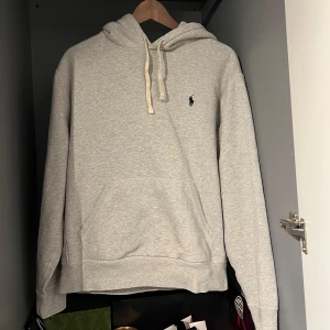 Grå hoodie från Ralph Lauren - Säljer en stilren grå hoodie från Ralph Lauren med en liten broderad logga på bröstet. Tröjan har en klassisk känguruficka och justerbar huva med snören. Perfekt för en avslappnad stil. Skriv vid funderingar eller frågor🙏🏽