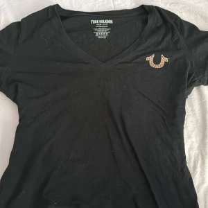 Svart t-shirt från True Religion - Vintage true religon tröja köpt i New York på en second hand butik. Står ingen storlek på tröjan men skulle säga att den är i storlek M. Jätte fina rosa stenar på tröjan.