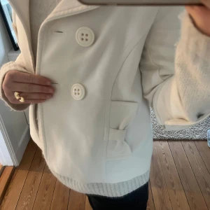Vit kappa med rosetter - Säljer en superfin kappa med 3/4 ärmar och dekorativa rosetter på fickorna och bak. Perfekt till våren💗passar xs-m. Som visat på sista bilderna finns några små noppror på tyget, med de är inget man tänker på💗