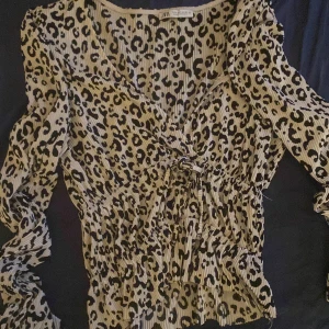 Leopardmönstrad blus från Zara - Trendig leopardmönstrad blus från Zara med v-ringning och knytning framtill. Blusen har långa ärmar och är tillverkad i ett lätt och luftigt material. Perfekt för att ge din outfit en djärv touch.