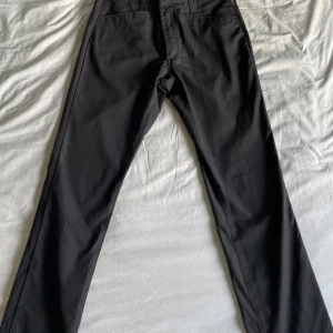 Svarta täckbyxor från Fjällräven -  Svarta täckbyxor från Fjällräven i en klassisk design. Byxorna har en rak passform. Aldrig anfvända utomhus. 