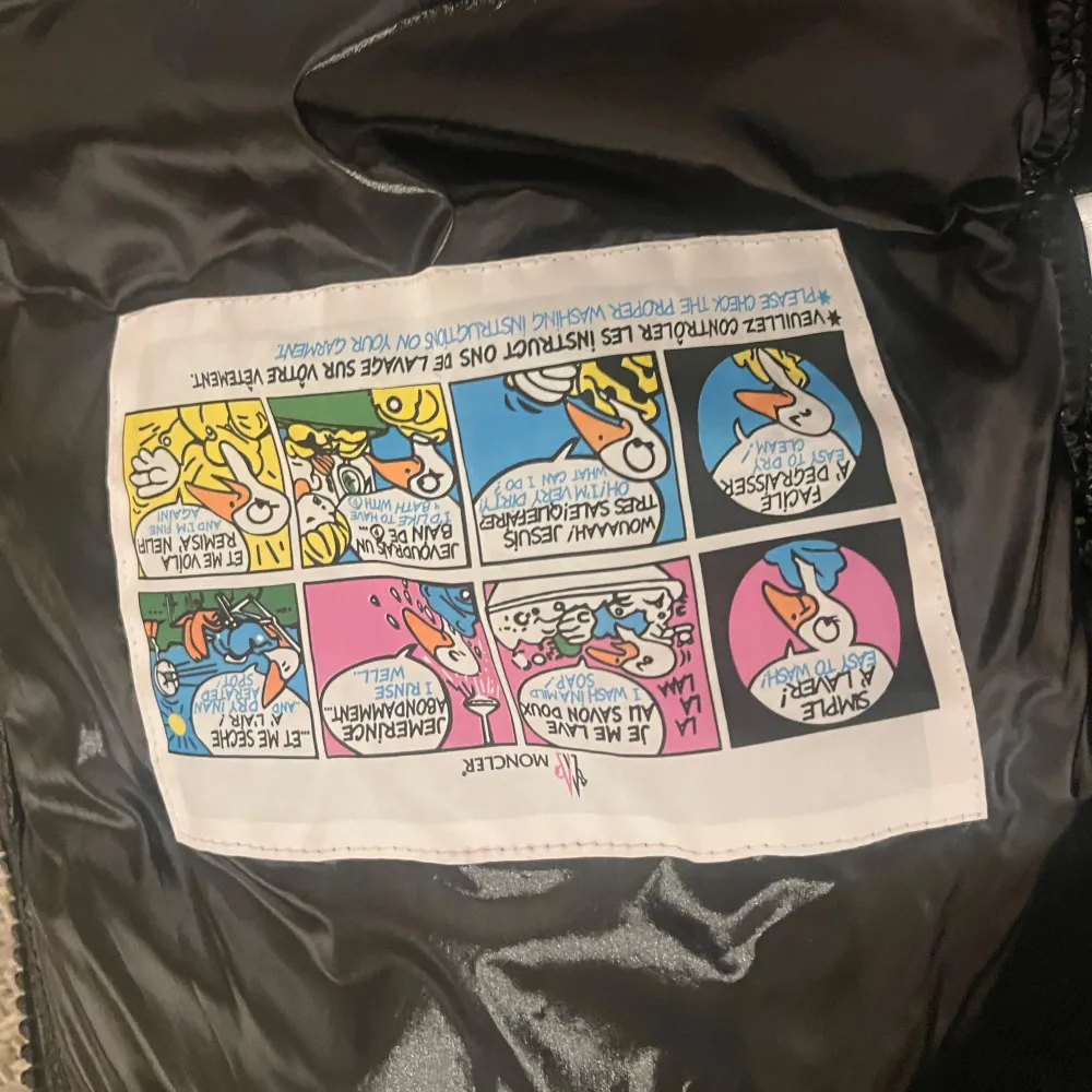 Snygg svart pufferjacka från Moncler med glansigt material och huva. Jackan har långa ärmar och dragkedja framtill. Det finns en ficka med knapp på ärmen och Moncler-loggan syns tydligt. Perfekt för kyligare dagar.. Takit.