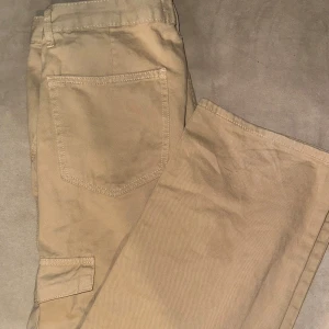Beige Cargo Byxor från Pull&Bear - Snygga beige cargo byxor från Pull&Bear med praktiska fickor på sidorna. Perfekta för en avslappnad stil. Tillverkade i ett skönt material. Ny skick endast provade