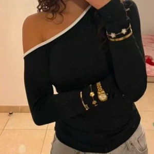 Svart oneshoulder topp - Snygg svart oneshoulder topp med lång ärm och vit kantdetalj. Perfekt för en stilren look.