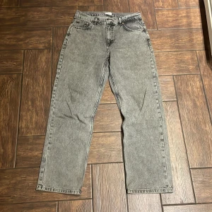 Grå jeans från Grunt - Snygga grå jeans från Grunt i en klassisk baggy fit. De har en midwaist design och är perfekta för en avslappnad stil. Jeansens midja är juster bar och är helt oanvänd 