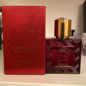 Versace Eros Flame Eau de Parfum - Säljer en elegant Versace Eros Flame Eau de Parfum i en djup röd flaska med guldlock. Flaskan har ett stilrent mönster och den ikoniska Versace-loggan. Perfekt för den som vill ha en doft med karaktär och stil.