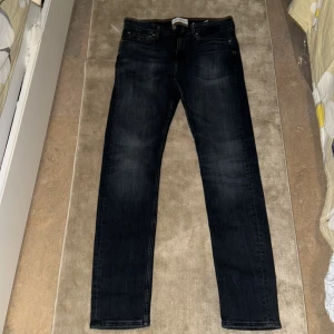 Mörk blåa jeansbyxor Calvin Klein slim taper - Snygga svarta jeansbyxor med en klassisk straight passform. De har en midwaist design och är perfekta för en stilren look. Byxorna har en dragkedja och knappar framtill.
