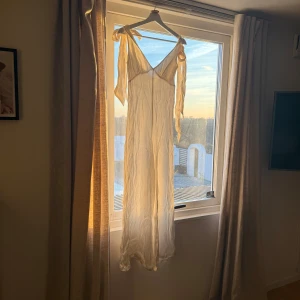 Vit jumpsuit i silke - Elegant vit jumpsuit med knytband vid axlarna. Klänningen har en luftig och romantisk design, perfekt för sommarens varma dagar. Den är tillverkad i ett lätt och flödande material som ger en vacker siluett.