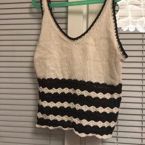 Randig stickad linnetopp - Snygg stickad linnetopp i beige och svart med randigt mönster. Toppen har en v-ringad design och är ärmlös, perfekt för varmare dagar. Den har en unik textur med spetsdetaljer som ger en extra touch. Det står storlek xs på lappen men skulle lätt passa en S också💕 köpt utomlands