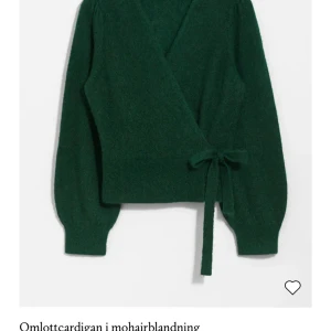 Grön omlottkofta i mohairblandning - Säljer en mysig grön omlottkofta i mohairblandning. Koftan har långa ärmar och ett knytband i midjan för en justerbar passform. Perfekt för kyligare dagar!