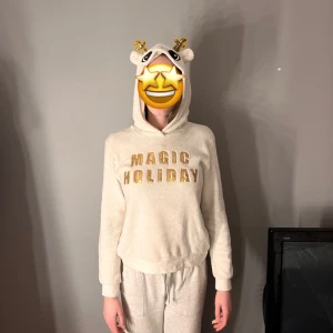 Vit hoodie med text och öron/ Jul tröja  - Mysig vit hoodie med texten 'MAGIC HOLIDAY' i guld på framsidan. Hoodien har en huva med söta öron och horn, vilket ger en lekfull touch. Perfekt för avslappnade dagar hemma eller som en rolig detalj i vardagslooken.