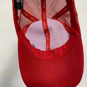 Röd keps från Polo - Snygg röd keps från Polo med nätpaneler för ventilation. Kepsen har en broderad logotyp på sidan och justerbar passform. Perfekt för en varm sommardag och sportig look.